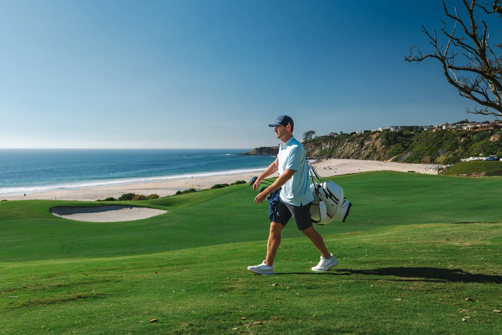 A golfer walking a coastal fairway with a bag over one shoulder