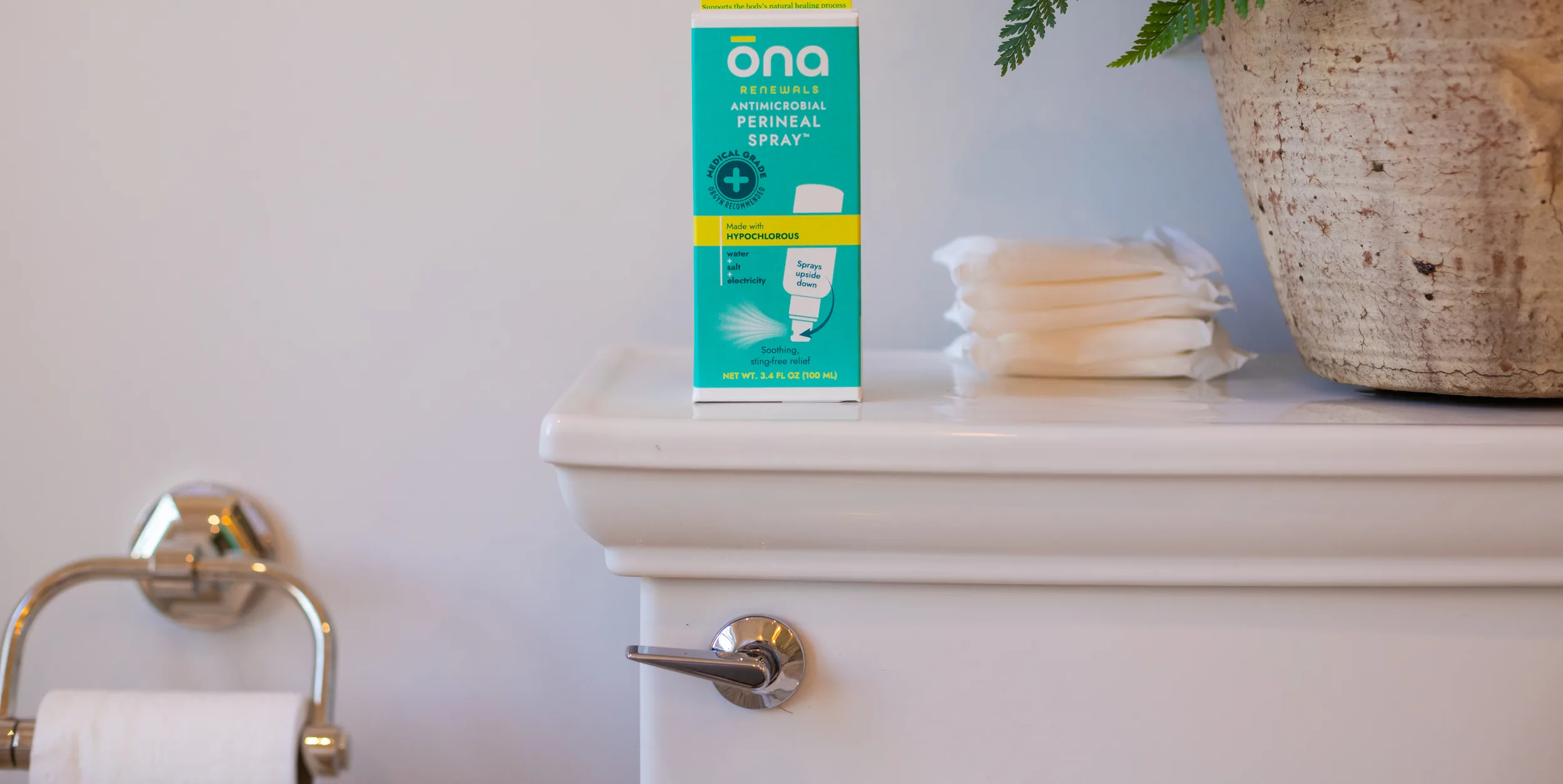 ōna postpartum product box on a bathroom shelf beside folded towels and a plant