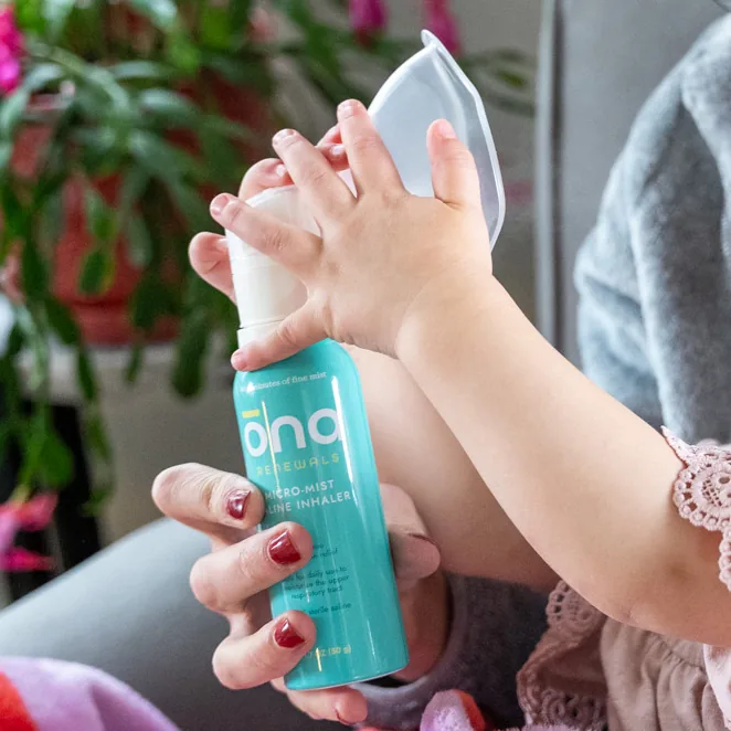 Parent's hand holding an ōna spray bottle beside a baby